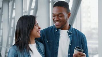 A couple of African American millennials share a joyful moment while waiting at the airport. They smile at each other, holding a coffee cup and enjoying their travel experience together. video