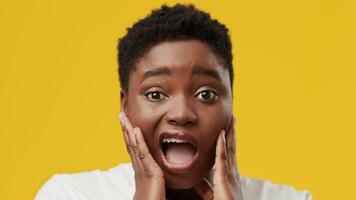 A young African American woman with a plump figure shows a surprised expression, hands on her cheeks, in a studio setting with a bright yellow backdrop, highlighting her joyful reaction. video