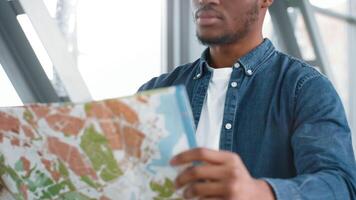 African American millennial man looks at a map while waiting in a busy airport, cropped video