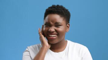 A young African American woman shows a pained expression while touching her ear in a studio setting. The bright blue background contrasts with her chubby features and emotional display. video