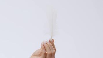 A young woman with clear skin enjoys a relaxing moment, gently stroking her face with a feather while practicing self-care. The minimalist background enhances the soothing atmosphere. video