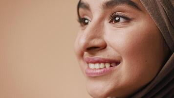 A young Arab woman in a hijab displays a warm smile, highlighting her features. The studio background is neutral, creating a serene and inviting atmosphere for the portrait. video