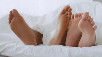 Couple cuddles in bed, showing love and affection with their feet intertwined. The soft bedding creates a cozy atmosphere for their intimate moment together. video