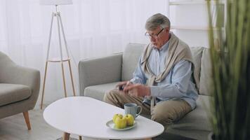 An elderly man sits comfortably in his living room, engaged in gaming with a controller. He enjoys a relaxed lifestyle while sipping coffee and watching apples on the table. video