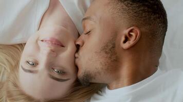 A young, multiracial couple cuddles closely in their bedroom, sharing smiles and affectionate glances while lying together in bed. The atmosphere is warm and loving, showcasing their bond. video
