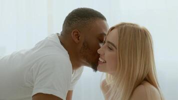 A young multiracial couple enjoys a moment of intimacy in their cozy bedroom. Their laughter and smiles reflect their deep connection and affection for each other. video