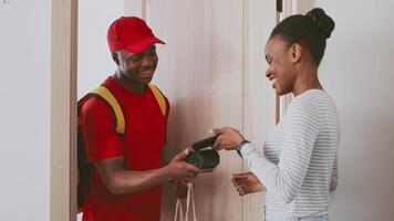 A man in a red shirt and cap delivers a package to a smiling woman at her apartment. The friendly interaction highlights the connection between courier services and customers. video