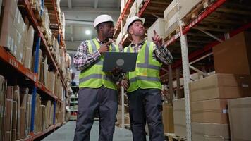 A warehouse manager discusses tasks with an employee while reviewing details on a laptop video