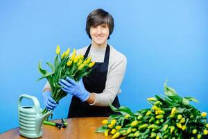 Pensioner lady florist wearing apron, working in flower shop studio and and making bouquet of tulips photo