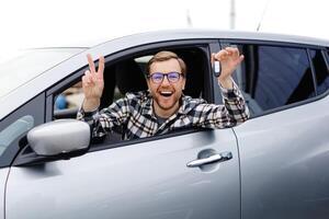 Excited man showing a car key, sitting inside his new vehicle photo