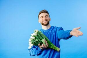 Man holding bouquet of tulips, looking at camera isolated on blue background. Celebration concept. photo