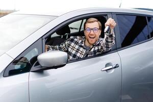 Excited young man showing a car key, sitting inside his new vehicle. photo