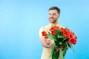Man holding bouquet of red tulips on blue background photo