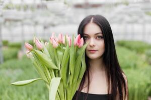 Young woman standing in large greenhouse and holding a blooming tulips in her hands. photo