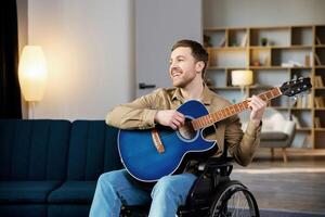 Handsome man with a disability sitting in wheelchair playing on guitar at home. photo
