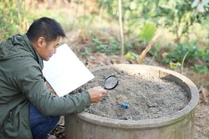 Asian man agronomist is inspecting and studying about quality of soil compost from sample soil in garden. Concept, soil quality inspection, research and develop for the best agriculture product. photo