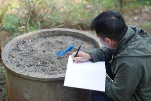 Asian man agronomist is inspecting and recording about quality of soil compost from sample soil in garden. Concept, soil quality inspection, research and develop for the best agriculture product. photo