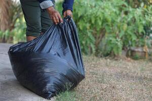 Closeup hand holds black plastic bag that contains garbage inside. Concept , Waste management. Environment problems. Daily chores. Throw away rubbish. Sorting type of garbage. photo