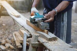 Carpenter using electric planer with wooden plank in carpentry worksite. Concept, tool or equipment for construction work. Using with careful and skillful for safety. photo