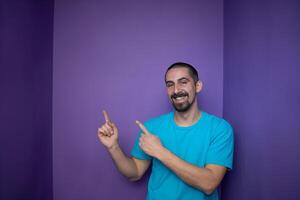 Smiling adult man introduce product, pointing finger against violet background with copy space. photo