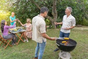 Friends cooking with the barbecue having a conversation smiling happy and laughing together talking in the patio. photo