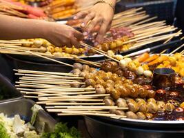 Stewed pot with meatballs and sausages skewers in hot spicy red sauce. Asian food Thailand. photo