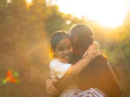 Mother and daughter are playing together in the park. Happy mother hugging her daughter sitting in the park with sunset light in nature. photo