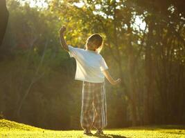 Happy little girl outdoors in nature and enjoying the trees with beautiful warm sunset in the park. photo