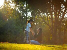 Mother and daughter are playing together in the park. Happy mother hugging her daughter sitting in the park with the sunset light. photo