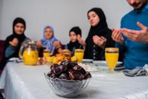 Happy Muslim family together making iftar dua to break fasting during Ramadan at the dining table at home focus on a bowl of dates healthy nutrition during the fast. photo