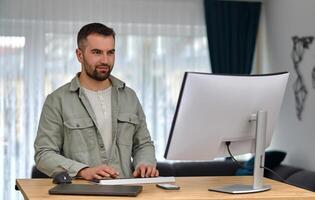 A happy man using a desktop computer while working at a home. photo