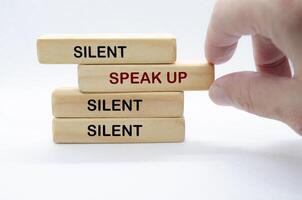 Hand pulling out wooden block with text saying SPEAK UP to separate from other wooden blocks with text SILENT. Courage and Speak Up concept. photo