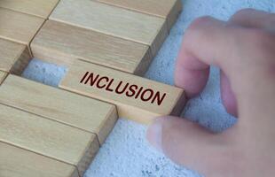 Hand placing Inclusion text on wooden blocks surrounded by other wooden blocks. D and I concept photo