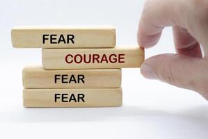 Hand pulling out wooden block with text saying COURAGE to separate from other wooden blocks with text FEAR. Courage and Speak Up concept photo