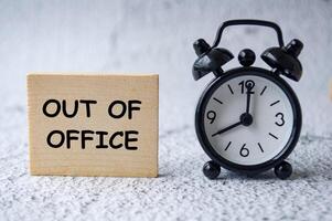 Out Of Office text on wooden square with table clock background photo