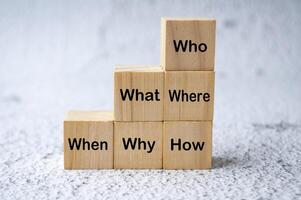 Who, What, Where, When, Why and How text on stacking wooden cubes. Fact finding concept photo