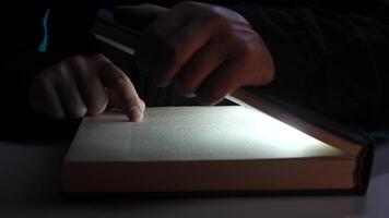 portrait curious Man reading book with flashlight in the dark. Light of the Holy Scripture video
