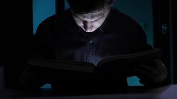 Man reading a book with a small light source in the dark. light from the book video