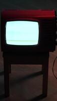 vertical Old red television displaying static noise on wooden stool in dark room video