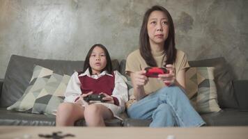 Asian family, mum, and kid fun playing console game with joy controllers on sofa in home living room together, enjoy and cheerful, happy weekend hobby of child and parent, digital entertainment. video