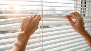 Adjusting white window blinds to control shadow play bright room interior close-up action shot photo