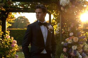A man in a tuxedo stands in front of a flower arch photo