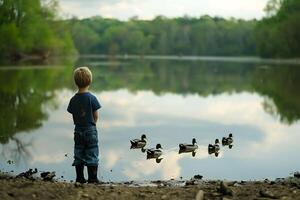 A boy stands near a lake with ducks photo