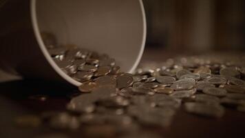 A number of scattered coins that have spilled from a cup resting on a wooden table video