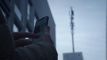 A person is using a smartphone while a cell tower is prominently visible in the background video