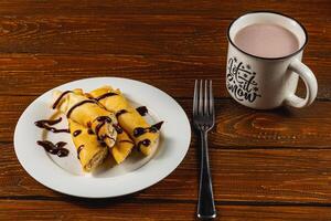 Sweet crepes drizzled with chocolate syrup served with hot cocoa photo