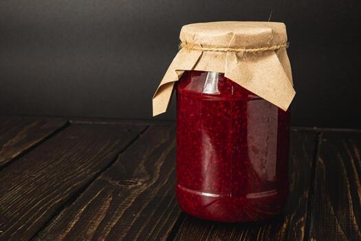 Homemade raspberry jam in a large jar with brown paper lid photo