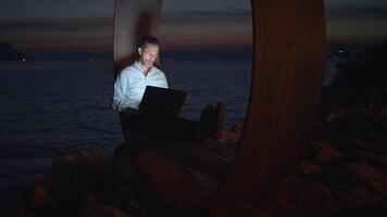 A man is diligently working on his laptop while enjoying the serene seaside at dusk video