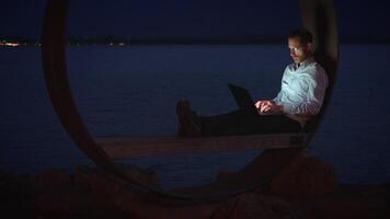 A Person Engaged in Work at Night by the Water While Seated in a Unique and Comfortable Spot video