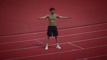 An athlete is seen stretching on the track field in preparation for their workout session video